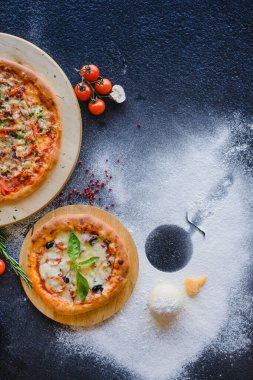 Restorandaki ahşap bir masada pizza fotoğrafı. Üst Manzara. Yakınlarda çeşitli malzemeler var: peynir, mantar, domates, baharat, un.