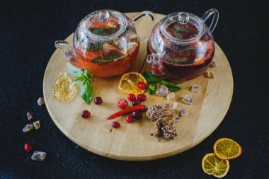 Lokantada siyah bir masanın üzerinde yuvarlak dokulu ahşap bir tahta üzerinde meyveli çay ile iki çaydanlık. Tatlıların yanında, şekerli meyveler.