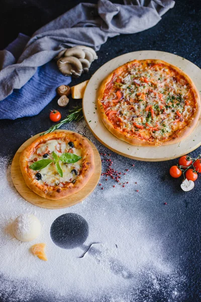Restorandaki ahşap bir masada pizza fotoğrafı. Yakınlarda çeşitli malzemeler var: peynir, mantar, domates, baharat, un..