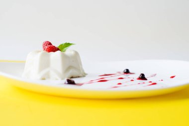 Beyaz bir tabakta jöleli kek ve sarı bir zemin üzerinde ahududu ve şurup.