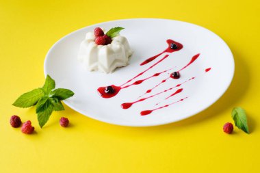 Ahududu, nane ve şuruplu beyaz bir tabakta kremalı pasta.