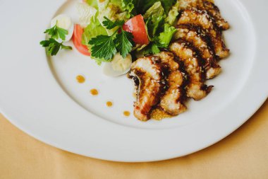 Restoranda masa örtüsüyle kaplı bir masada bir tabak servis edilir. İçinde balık, alet, sos olan bir tabak. Makro