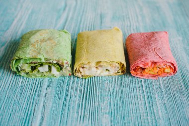 Shawarma parlak sarı, kırmızı, yeşil lahanalı sebze ve eti dokulu mavi ahşap bir masada. Kes.
