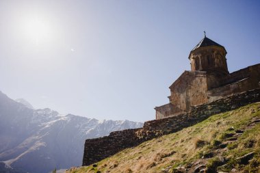 Mavi gökyüzü ve kilisesi olan güzel bir dağ manzarası. Gürcistan 'daki Kazbek Dağı' nın karla kaplı zirvesi