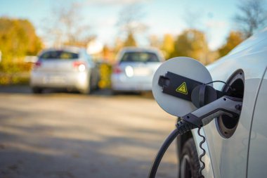 Şarj istasyonunda elektrik kablosu olan EV Car ya da elektrikli araba yumuşak ışıklı arka planı olan bulanık doğaya takılı..