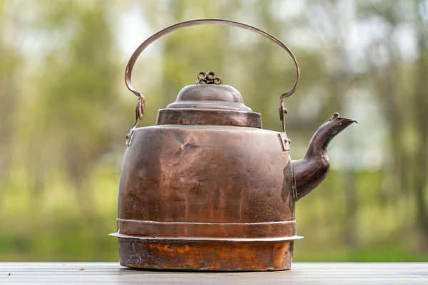 Image of Old copper kettle on the wooden table with trees at the background