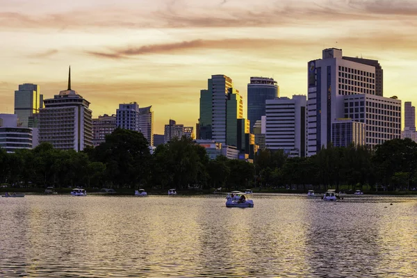 Nature lake in public park at city center with business buildings and sunset sky background, Bangkok, Thailand