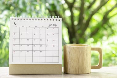 Haziran ayı, Takvim masası 2022 planlama ve ahşap kahve fincanı yeşil doğa arka planlı ahşap masa üzerinde.