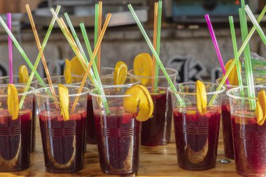 foreground in horizontal view of a row of sangria glasses with orange slices and colored drinking straws.sangria is a refreshing drink native to Spain and Portugal