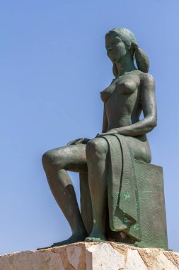 Bronz heykel, havlusuyla oturan bir banyoyu temsil eden kadına hürmet ediyor. Heykel Campello 'nun Alicia belediyesindeki Paseo de la voramar de les escultures' da yer almaktadır.