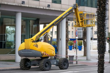 Sokakta boş sepeti olan sarı renkli eklemli bir kaldırma aracının yatay görüntüsü. 