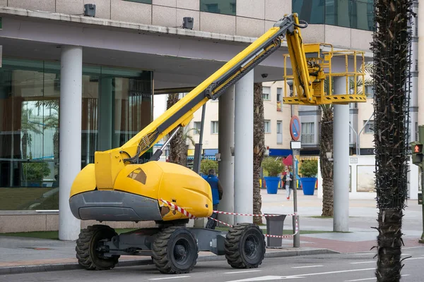Sokakta boş sepeti olan sarı renkli eklemli bir kaldırma aracının yatay görüntüsü. 