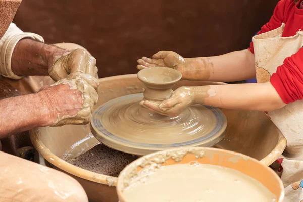 closeup in horizontal view of the hands of a potter and a girl while the potter teaches the girl to model a clay cup. apprenticeship of traditional trades