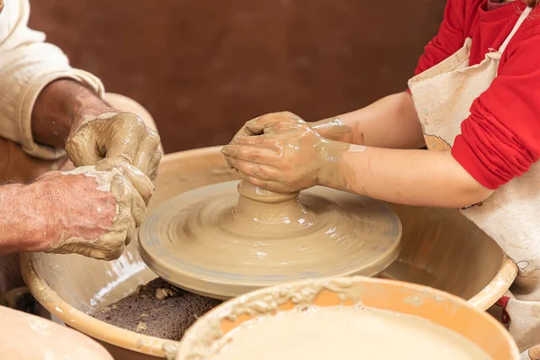 closeup in horizontal view of the hands of a potter and a girl while the potter teaches the girl to model a clay cup. apprenticeship of traditional trades