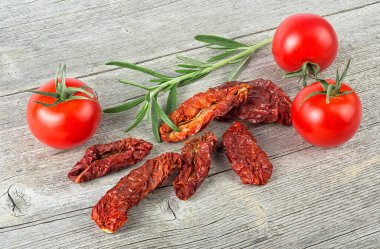 Geleneksel Akdeniz mutfağı - taze domatesli lezzetli kurutulmuş domatesler ve ahşap masa üzerinde biberiye dalı.