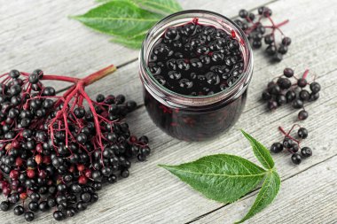 Cam kavanozda nefis ev yapımı siyah mürver şurubu ve ahşap masa üzerinde yeşil yapraklı bir demet siyah mürver.