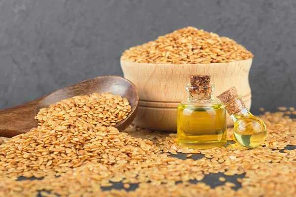 Tahta kaşıkta keten tohumu ve siyah taş masada cam şişelerde keten yağı. Sağlıklı yiyecek ve içecek konsepti.