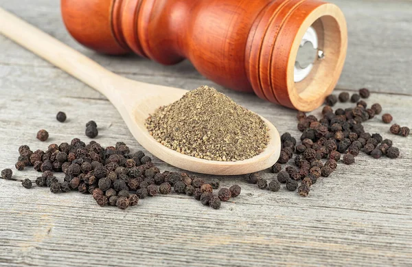 Wooden pepper mill, black peppercorns and ground black pepper on old wooden table.