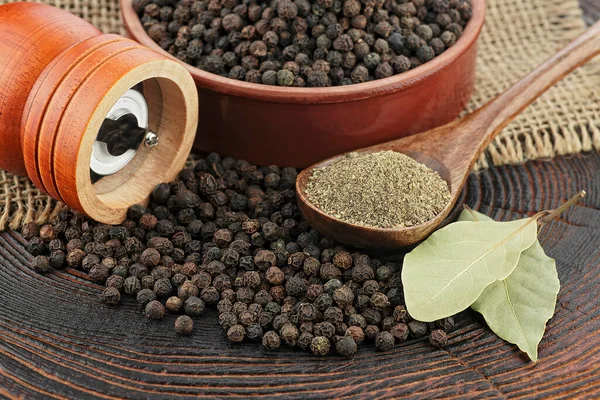 Wooden pepper mill, laurel leaves, black peppercorns and ground black pepper on old wooden table.