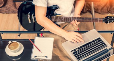 Erkek besteci, söz yazarı, ev stüdyosunda siyah elektro gitar çalarken dizüstü bilgisayarda müzik düzenlemeyi seviyor. şarkı yazma konsepti