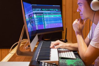 Asyalı müzik yapımcısı Midi klavyesinde ve masaüstü bilgisayarında ev stüdyosunda bir şarkı ayarlıyor. müzik üretim teknolojisi kavramı