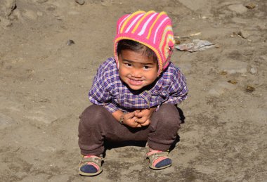 küçük Nepalce çocuk gülümser ve zemin üzerinde oturur.