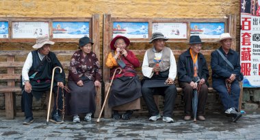 LHASA, Tibet, Çin - 17 Ağustos 2018: Geleneksel giysiler içinde yaşlı Tibetliler Jokhang Tapınağı yakınlarındaki bir bankta oturuyorlar