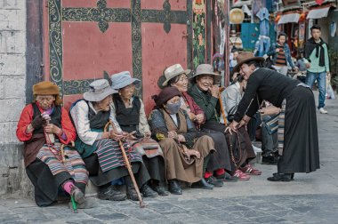 LHASA, Tibet, Çin - 18 Ağustos 2018: Geleneksel giysiler içinde yaşlı Tibet halkı Jokhang Tapınağı yakınlarındaki bir bankta oturuyor