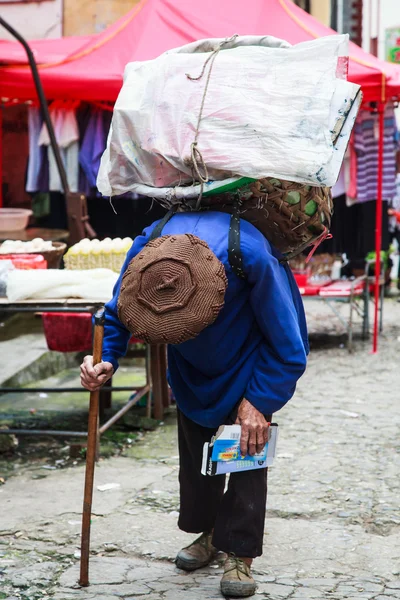 Oude gebogen man lopen met een mand op zijn rug — Stockfoto