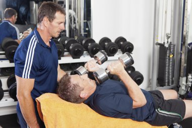 Senior male being spotted by personal trainer clipart