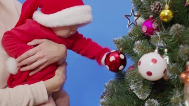 Anne bebeğiyle Noel ağacının yanında. Anne ve bebek yeni yıl ağacı ile oynuyorlar..