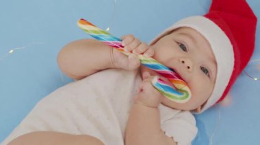 Noel Baba şapkalı, kırmızı elbiseli, beyaz yumuşak yatakta oynayan yeni doğmuş komik bebek tatlı yala. Noel tatili kavramı, şekerler, mutlu yıllar, bebekler, çocukluk. Yakın plan.,