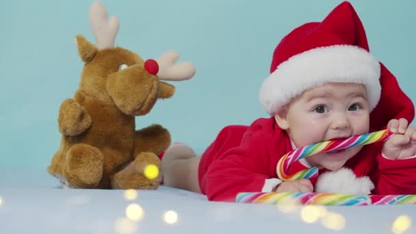 Veselé Vánoce, šťastný nový rok, kojenci, dětství, dovolená koncept - close-up úsměv legrační novorozeně v Santa Claus klobouk, červená bodysuit hrát na bílé měkké posteli lízat sladké vánoční cukroví.