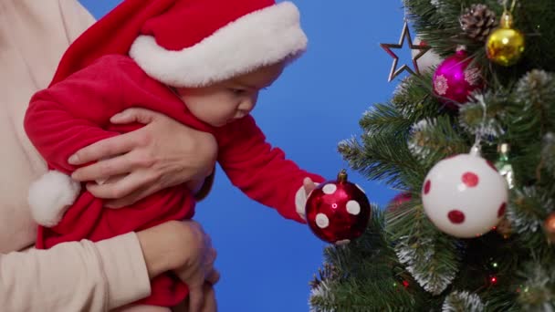 Madre con su bebé cerca del árbol de Navidad. Madre con niña jugando con árbol de año nuevo. — Vídeo de stock
