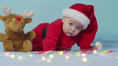 Mutlu Noeller, mutlu yıllar, bebekler, çocukluk, tatil konsepti - yakın plan gülümseyen yeni doğmuş bebek Noel Baba şapkalı, kırmızı beden beyaz yumuşak yatakta oynuyor.