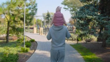 Baba oğul parkta yürüyor. Çocuk ebeveynin üzerinde oturuyor..