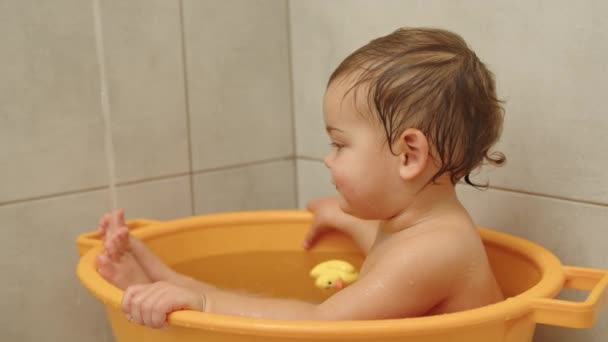 Lassú mozgású videó aranyos kislány ül és mosolyog a fürdőben. — Stock videók