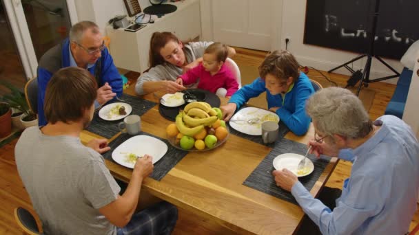 Wysoki kąt widzenia dużej wielopokoleniowej rodziny siedzi razem przy stole, kładąc jedzenie na talerzach i wlewając napoje do kieliszków podczas świątecznej kolacji w domu — Wideo stockowe