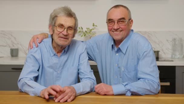Портрет двух белых стариков, сидящих, обнимающихся и улыбающихся перед камерой перед камерой в доме. — стоковое видео