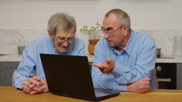 Senior mogna äldre män som använder en bärbar dator medan du kopplar av hemma — Stockvideo