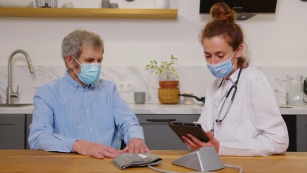 Visitatore sanitario e un uomo anziano durante la visita a casa. Un'infermiera o un medico che esamina un uomo . — Video Stock