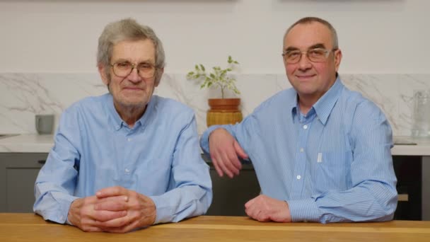 Retrato de los dos ancianos caucásicos sentados, abrazando y sonriendo a la cámara delante de la cámara en la casa. — Vídeo de stock