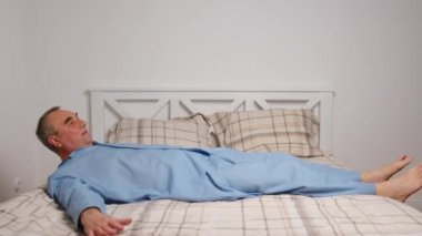 Mutlu, hayat dolu yaşlı adam rahat yatak egzersizleri yapıyor. Gülümseyen, emekli, esneyen, yatak odasında uzanan, enerji dolu, günaydın konseptinin keyfini çıkaran,.