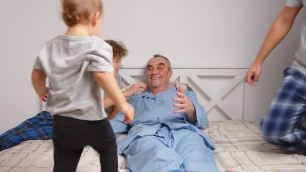 Paciente varón anciano abrazando a los niños y hablando mientras está acostado en la cama en casa — Vídeo de stock