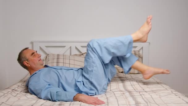 Šťastný živý starší muž dělá cvičení pohodlné postele. Usmívající se zdravý důchodce starší muž protahování sedí v ložnici pocit plné energie těší dobrou ranní koncepci. — Stock video