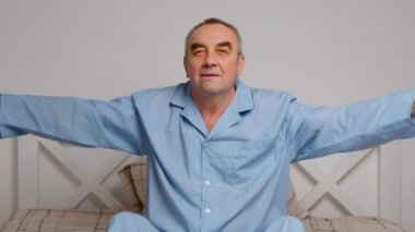 Mutlu, hayat dolu yaşlı adam rahat yatak egzersizleri yapıyor. Gülümseyen, emekli, esneyen, yatak odasında uzanan, enerji dolu, günaydın konseptinin keyfini çıkaran,.