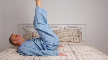 Mutlu, hayat dolu yaşlı adam rahat yatak egzersizleri yapıyor. Gülümseyen, emekli, esneyen, yatak odasında uzanan, enerji dolu, günaydın konseptinin keyfini çıkaran,.