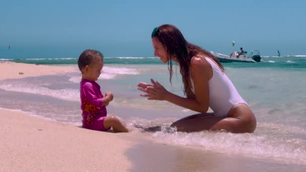 母親と娘がビーチに座っている。若いですcaucasian家族の母親女の子笑顔遊びカジュアルな旅行ライフスタイルリラクゼーションパラダイスビーチ海愛する — ストック動画