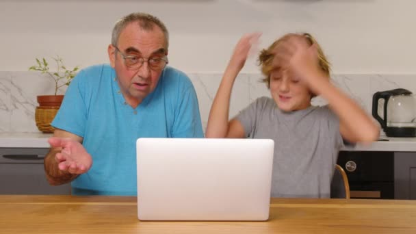 Szczęśliwe pokolenie stary dziadek i chłopiec siedzą razem przy laptopie w kuchni. Dzieci uczą osoby starsze pracy na laptopie — Wideo stockowe