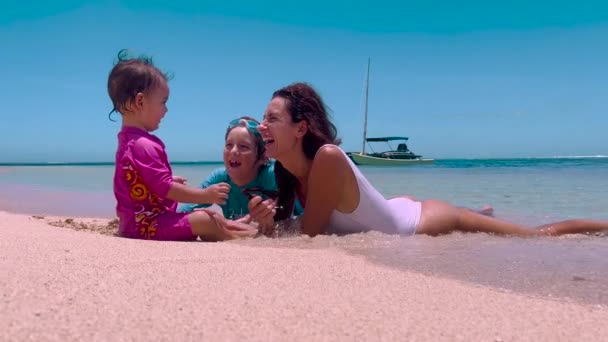 母親と子供たちはビーチに座っています。若いですcaucasian家族の母親女の子と男の子笑顔再生カジュアルな旅行ライフスタイルリラクゼーションパラダイスビーチ海愛する — ストック動画